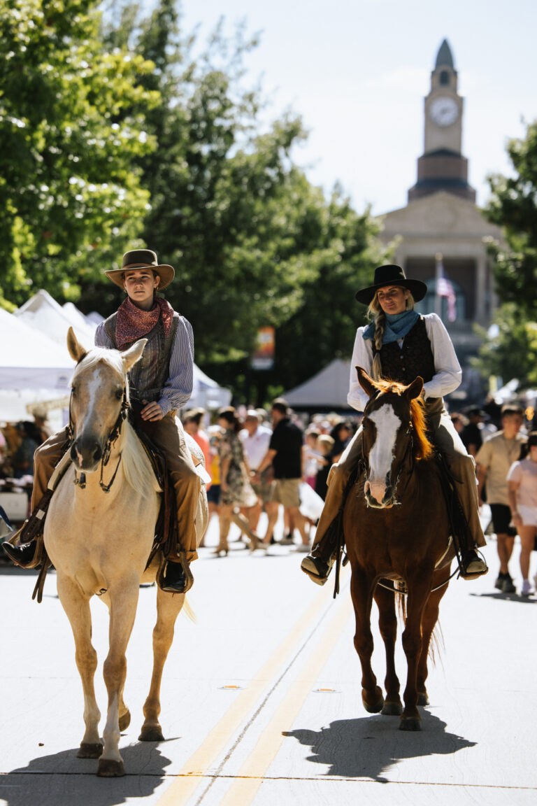 A man and a woman ride a horse along a road past a small crowd