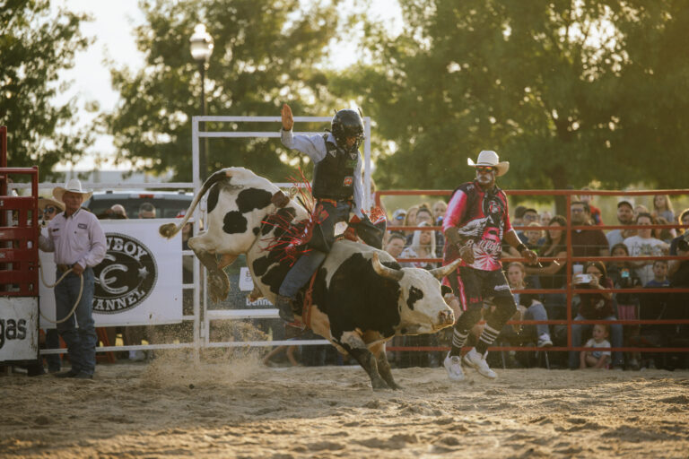 A man wearing a helmet is riding a bucking bull in front of the crowd
