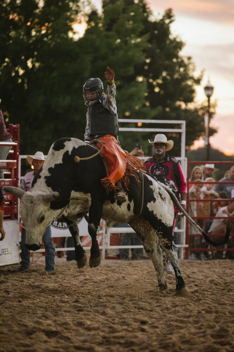A man balances on a bucking bull that is mid-air