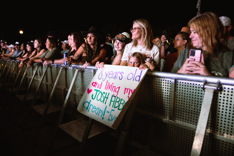 A mother and daughter hold a poster in front of the crowd at a concert