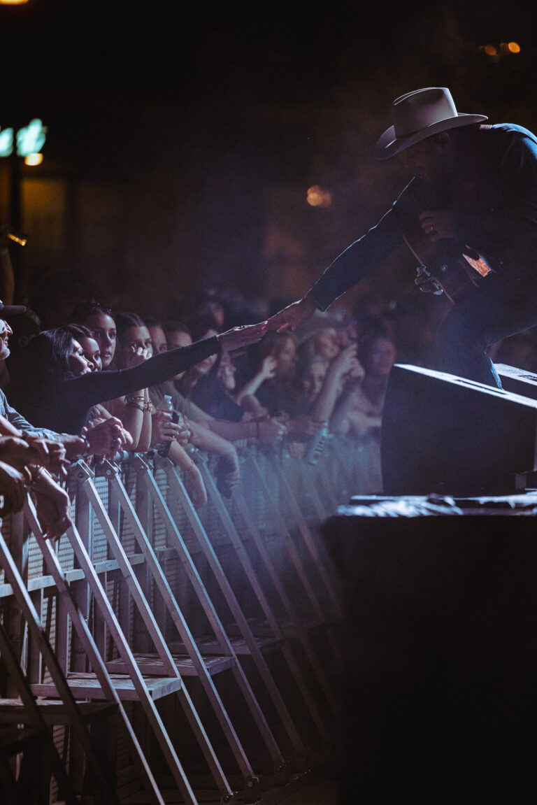 A singer reaches down from the stage to touch a fan's hand in the crowd