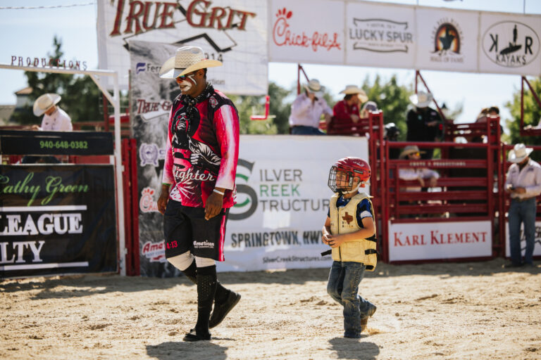 An event organizer is walking with a boy who is wearing a helmet and a safety vest